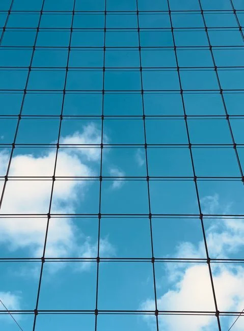 Two workers clean windows on a tall office building in a city setting.