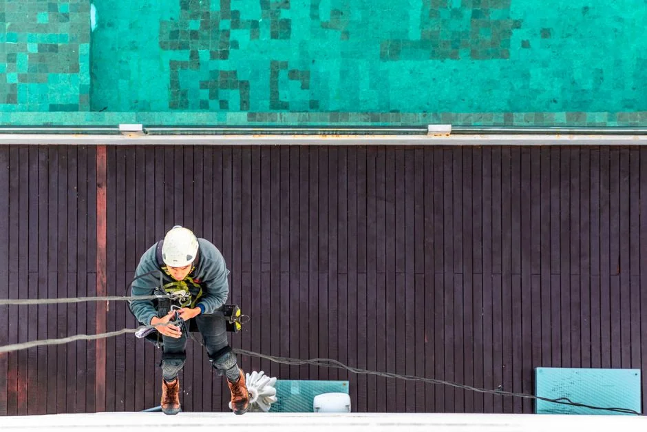 A male window cleaner washing the exterior glass roof from above with a tool during daylight.